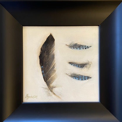 Framed wall art featuring a feather sketch on an off-white background, with three blue-gray feather illustrations on the right and a black frame mounted on a light textured wall.