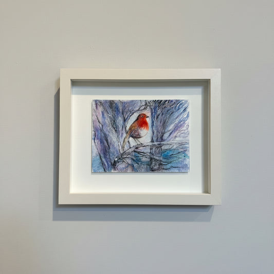 Framed artwork of a bird on a branch against a blue sky, displayed on a wall.