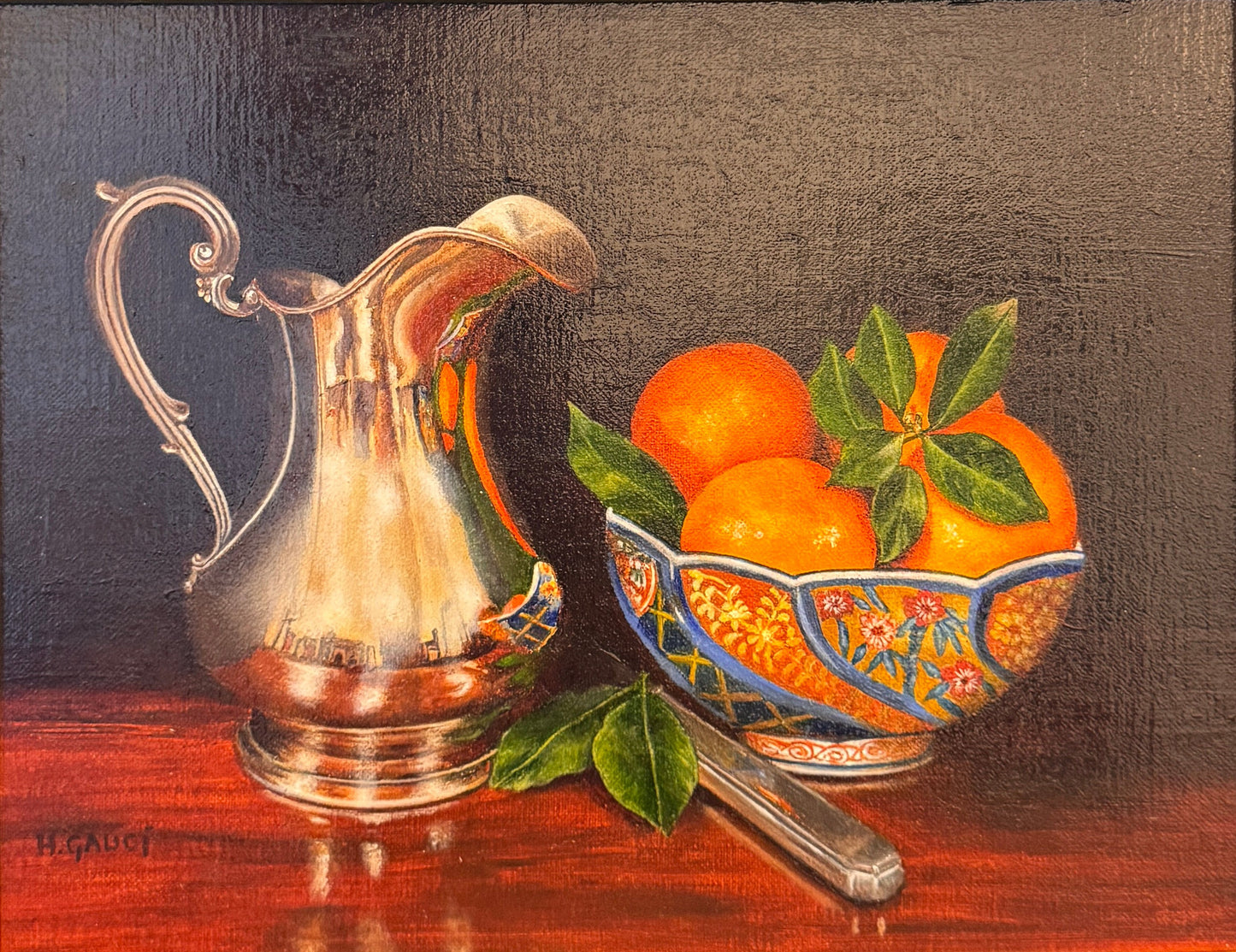 Framed still life painting with a silver pitcher and bowl of oranges on a textured surface.