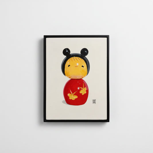 Framed artwork of a traditional Japanese kokeshi doll with black hair and red body on a white background