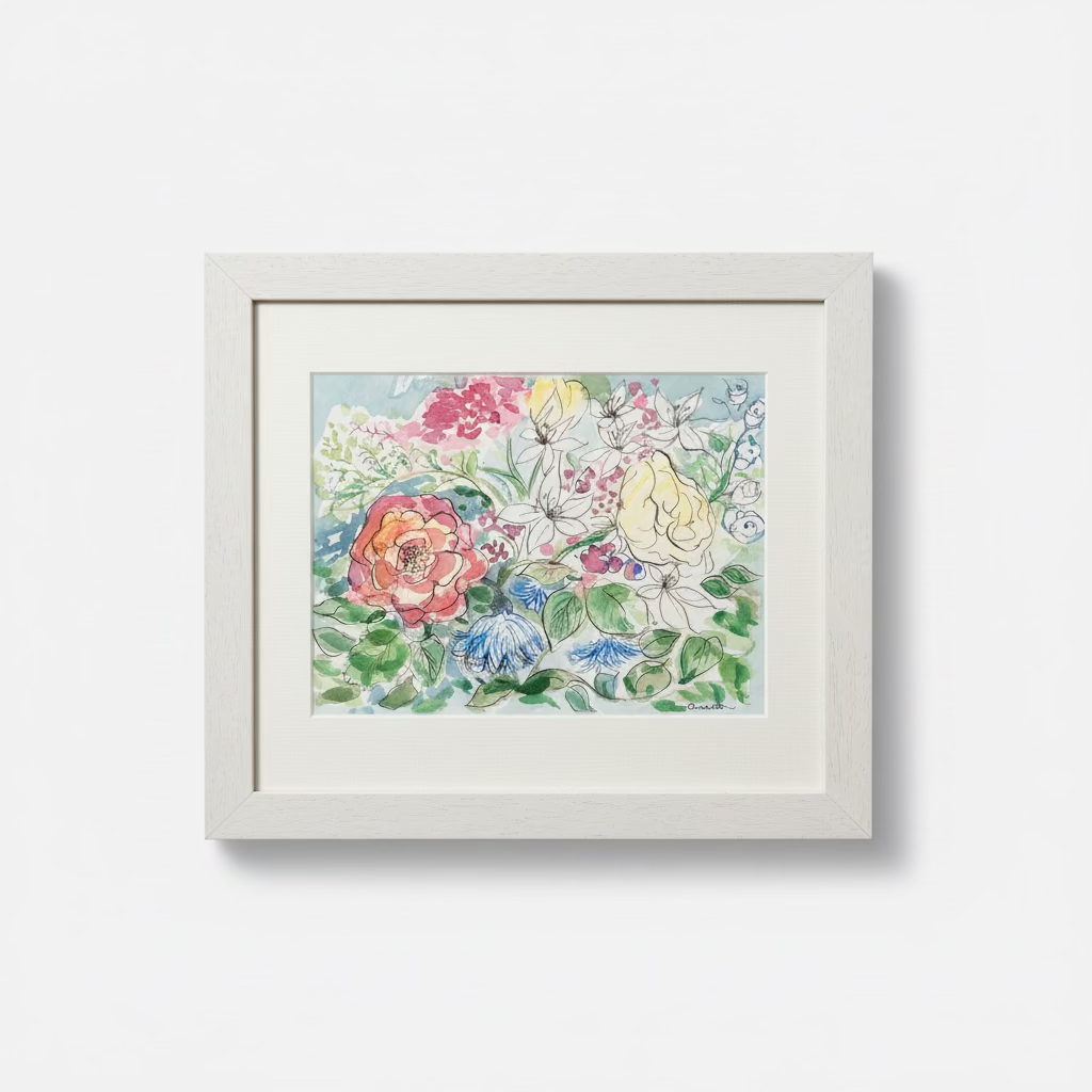 A framed watercolor painting of a colorful garden floral bouquet, set in a light beige frame and resting on a white surface against a textured beige wall.