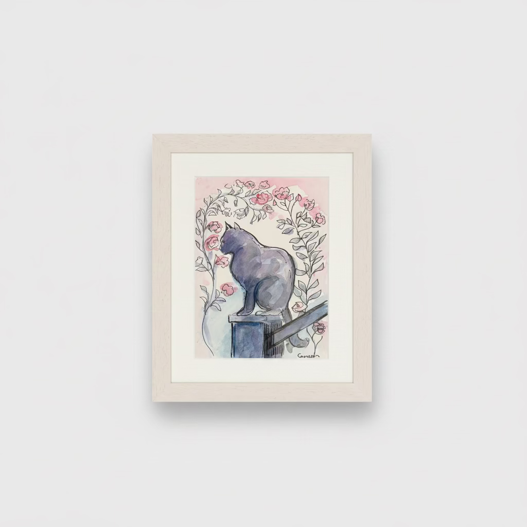A framed art print featuring a watercolor illustration of a black cat sitting on a pedestal among pink roses, displayed on a white surface against a textured beige wall.