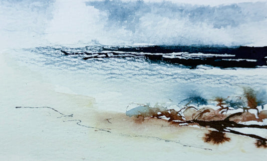 Watercolor landscape painting of a beach scene with dark rocky shoreline, misty blue-gray sky, pale sandy foreground, and brown seaweed or driftwood in the lower right.