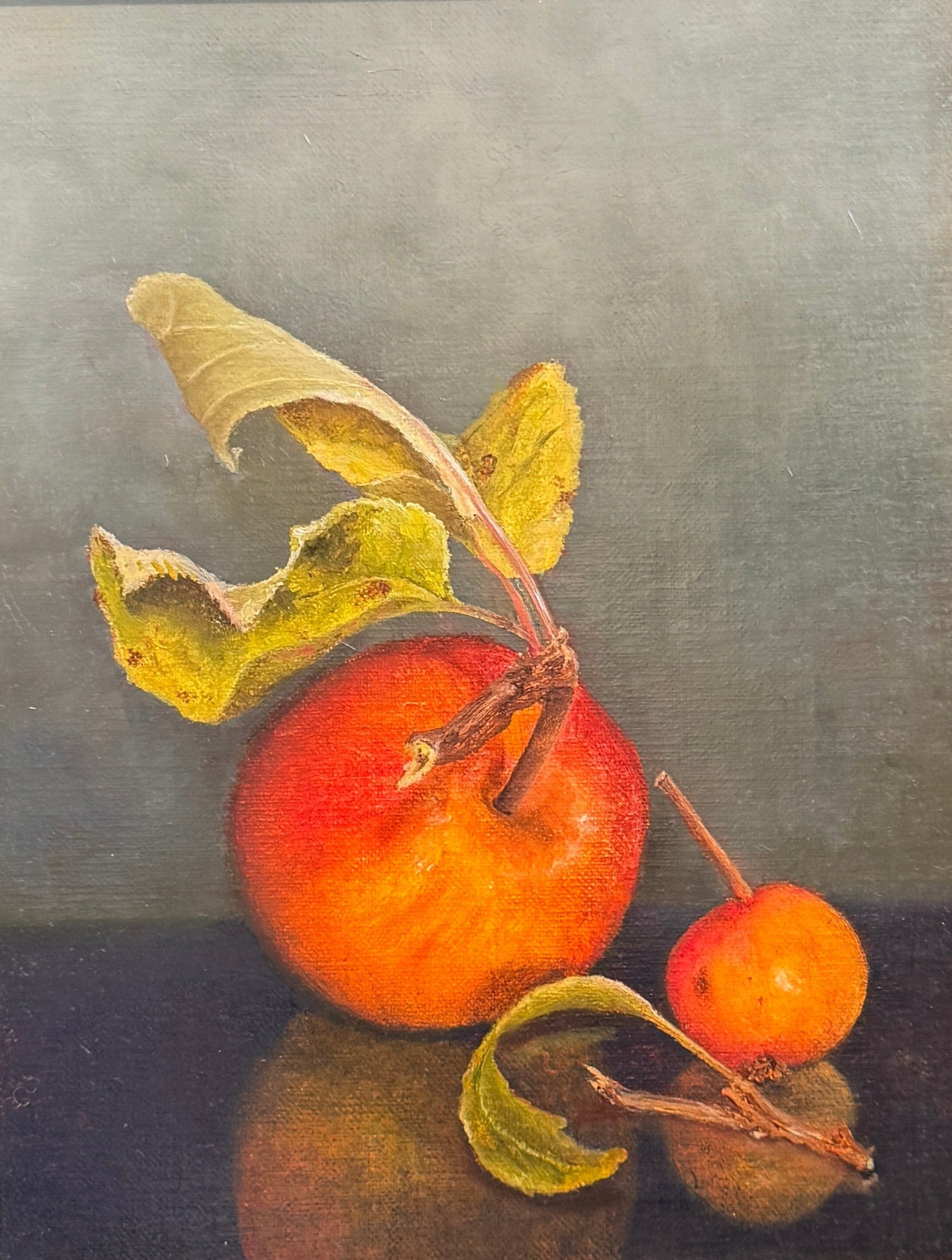 Framed still life painting of an apple and leaves on a textured wall.