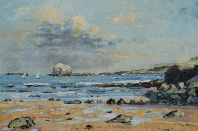 An impressionistic landscape painting of a rocky coastal beach with blue water, a pale sandy shore, dark rocks, distant sailboats, and a cloudy sky with soft yellow highlights.