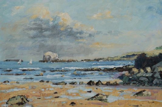 An impressionistic landscape painting of a rocky coastal beach with blue water, a pale sandy shore, dark rocks, distant sailboats, and a cloudy sky with soft yellow highlights.