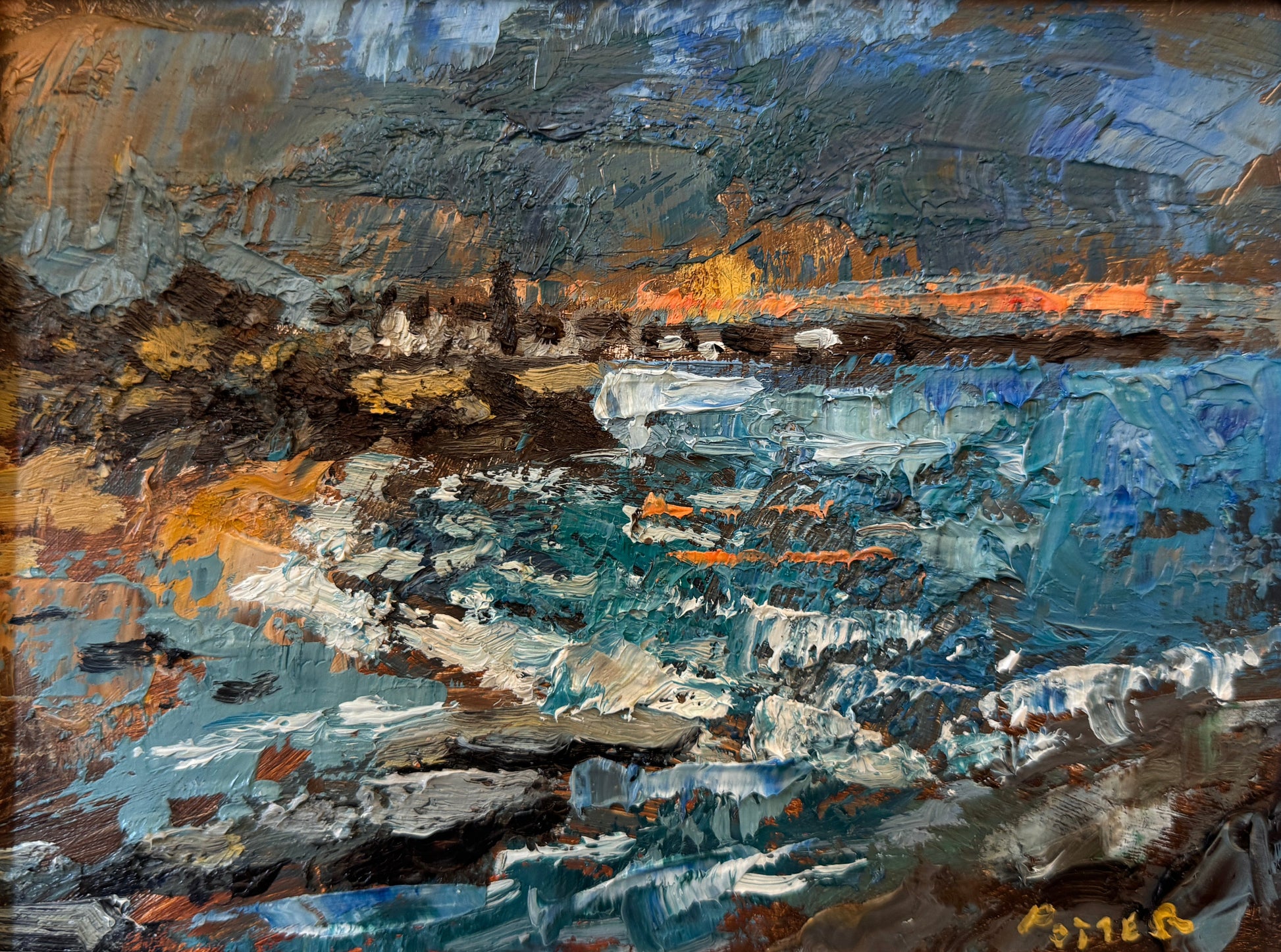 An impressionistic landscape oil painting of a rocky coastline with blue and white waves, dark cliffs, and warm orange highlights under a stormy sky, housed in a light natural wood frame.