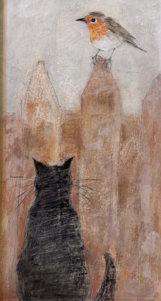 A framed painting depicting a black cat from behind looking up at a small robin perched on a fence, set in a light natural wood frame against a textured beige wall.