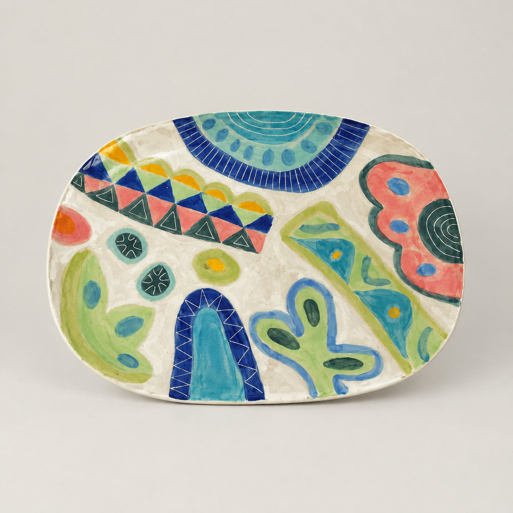 A ceramic serving platter with an abstract, colorful pattern of blue, green, pink, and yellow shapes on a white base, displayed inside a white box.