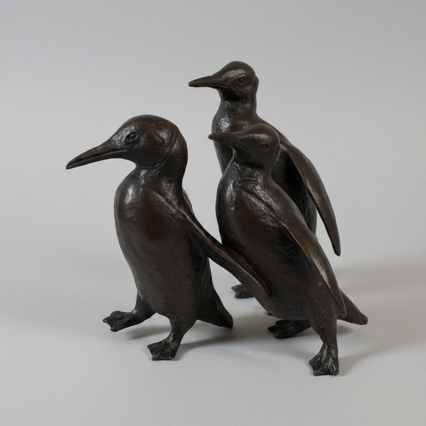 Sculpture of three bronze penguins on a textured white surface