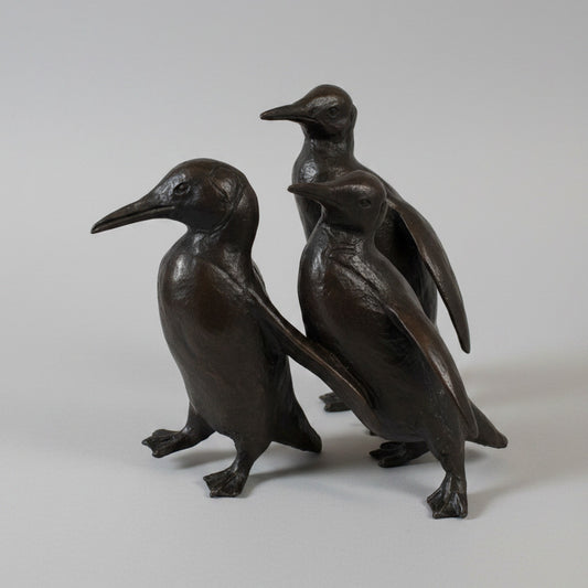 Sculpture of three bronze penguins on a textured white surface