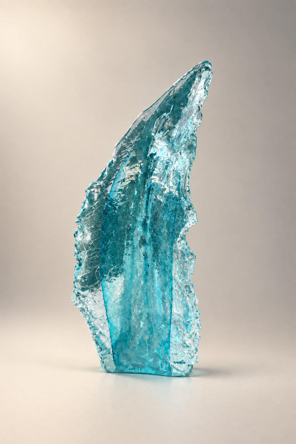 A tall, translucent light blue glass sculpture standing on a white pedestal in an indoor gallery or studio space with framed artwork on the wall behind it.