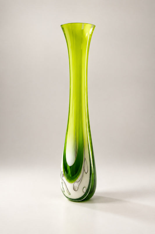 A tall, flared glass vase with a vibrant lime green and dark green gradient and a white swirl pattern near the base, displayed on a white table in an art gallery.
