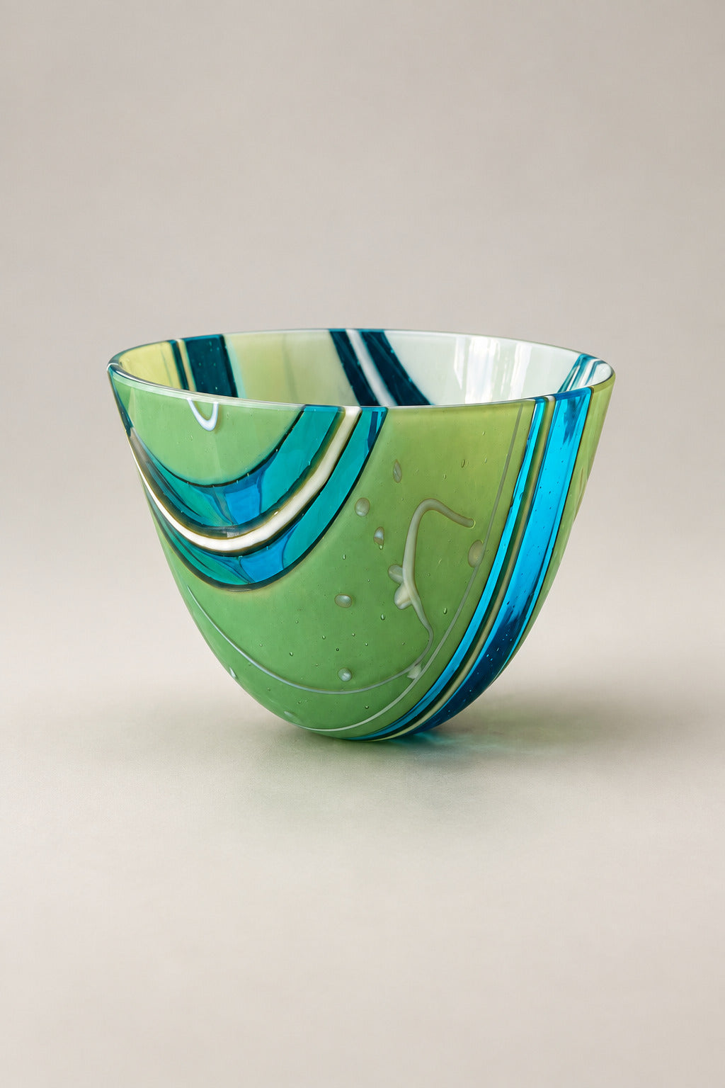 A hand-blown glass bowl with green, blue, and white swirls, sitting on a polished green marble table in an indoor setting.