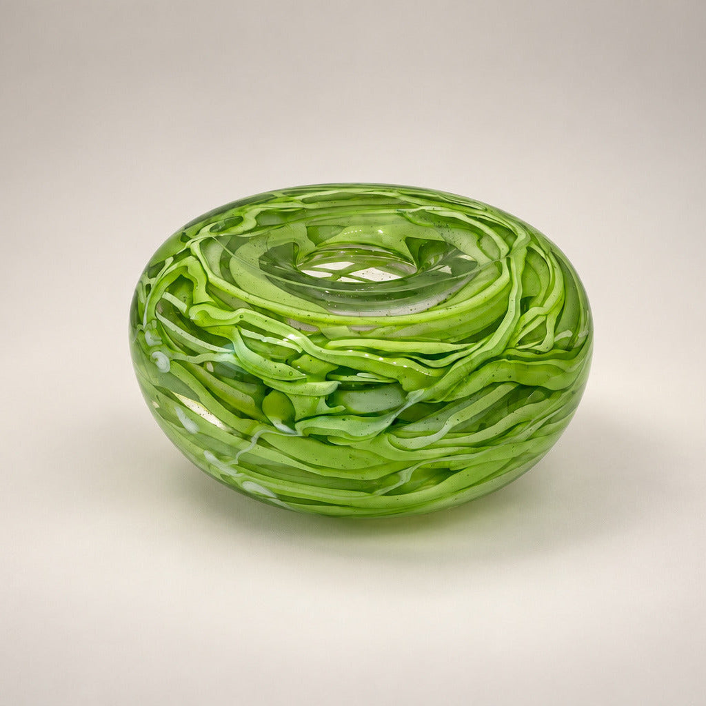 A small round glass bowl with a swirled, marbled green pattern, sitting on a white surface against a textured beige wall.