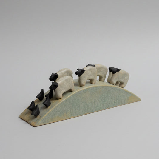 Ceramic sheep figurines on a curved base against a textured wall.