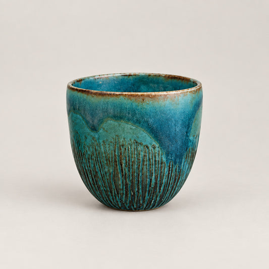 small ceramic bowl displayed on a glass shelf against a textured off-white wall.