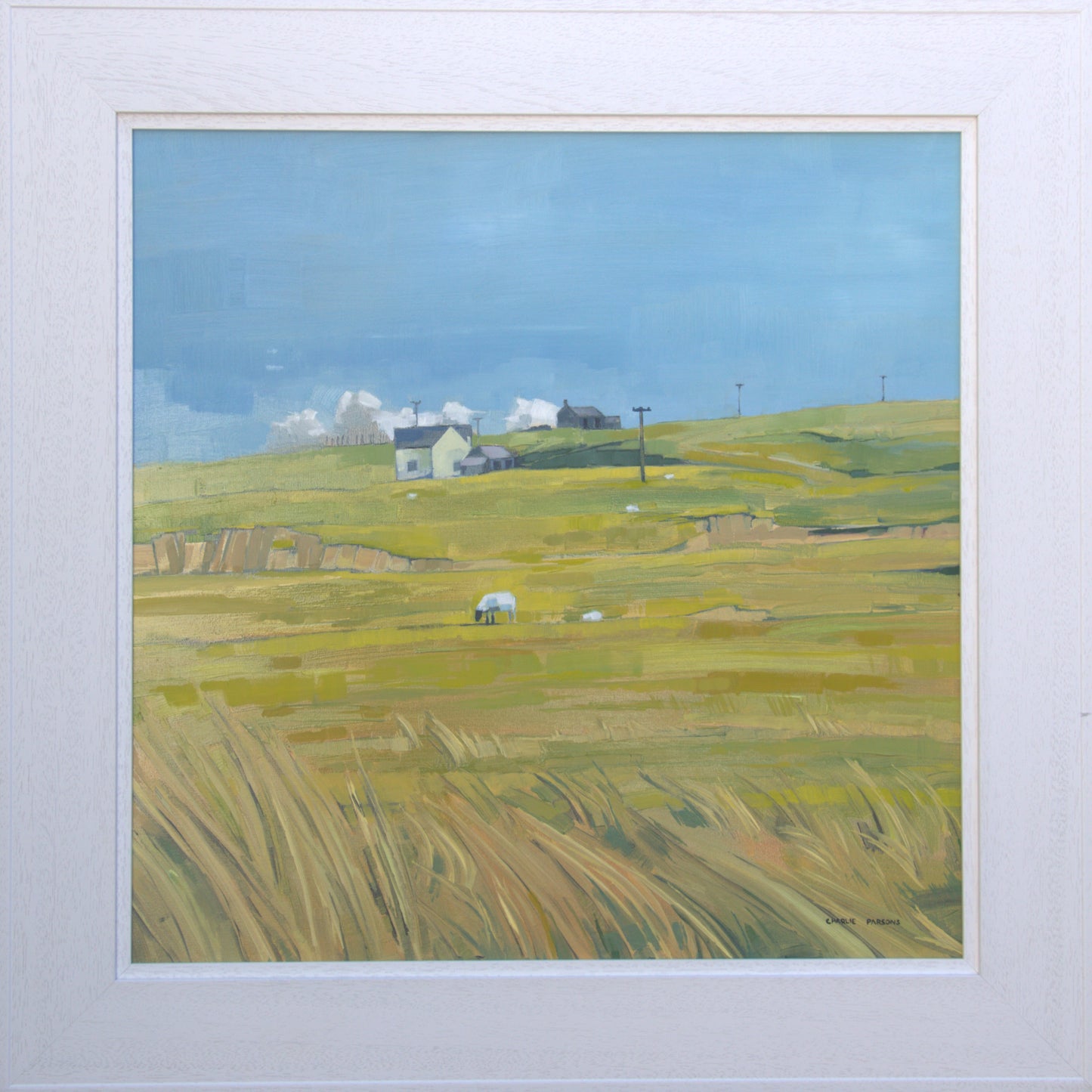 Framed artwork of a landscape with green fields and houses under a blue sky.