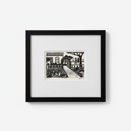 A framed black and white art print depicting a stylized garden scene with a path, trees, and architectural details, set in a black frame with a white mat against a light gray background.