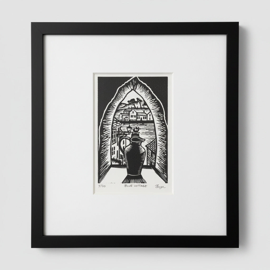 A framed black and white art print featuring a block-print style illustration of a house seen through an arched doorway with a large vase in the foreground. The print is matted in white and enclosed in a black frame, shown against a light gray wall.