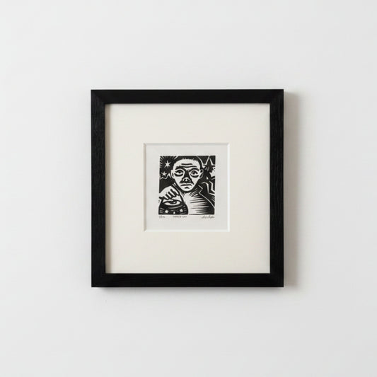 A framed black and white art print featuring a stylized portrait of a woman, mounted with a wide white mat inside a black frame against a light gray wall.