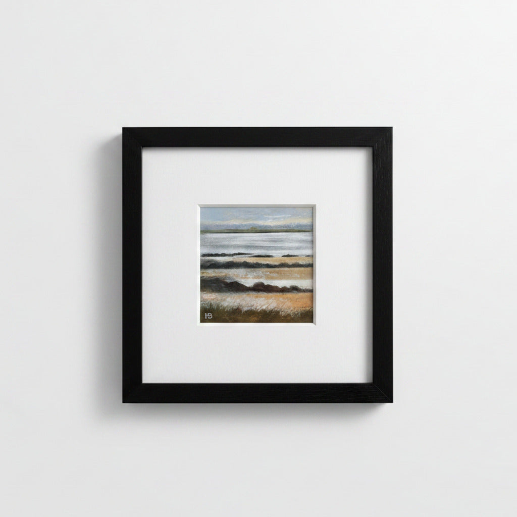 A framed landscape art print featuring a beach scene with muted blue-gray and beige tones, presented in a black frame with a white mat against a light gray wall.