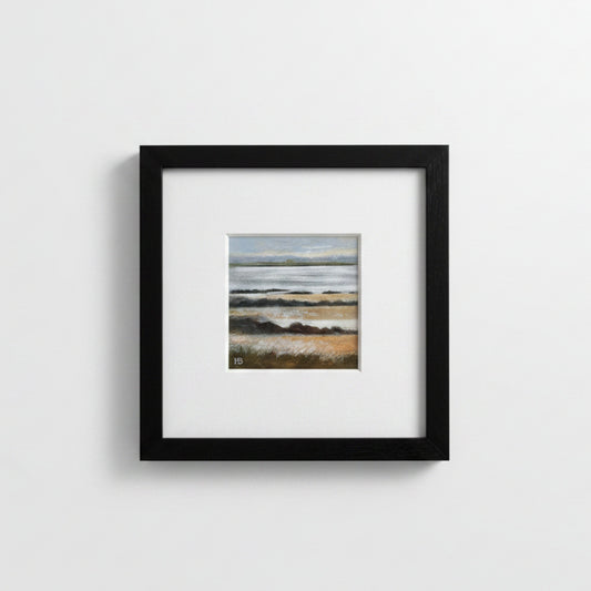 A framed landscape art print featuring a beach scene with muted blue-gray and beige tones, presented in a black frame with a white mat against a light gray wall.