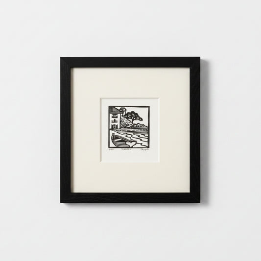 A framed black and white art print featuring a minimalist block-style illustration of a house and tree, set against a clean white background.