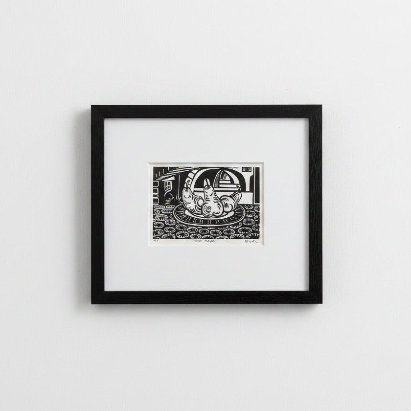 A framed black and white art print featuring a whimsical illustration of a rabbit on a plate, displayed on a clean white wall.