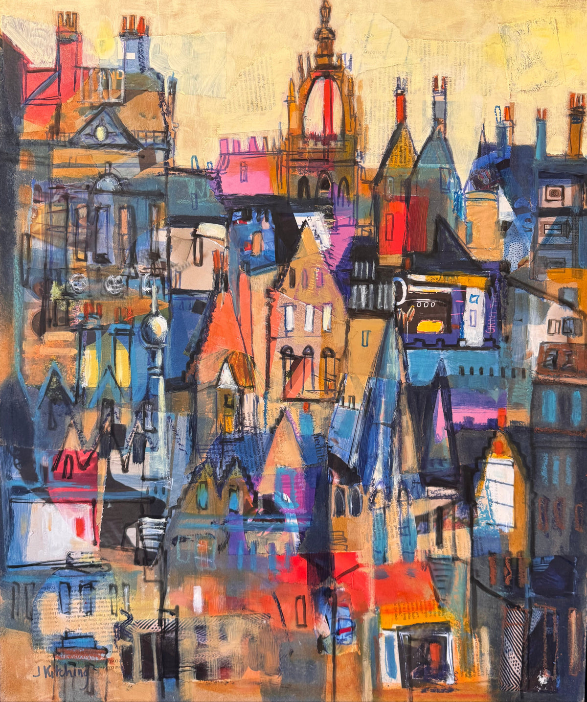 A framed abstract painting of a dense cityscape with colorful rooftops and buildings, shown leaning against a wall on a dark surface.