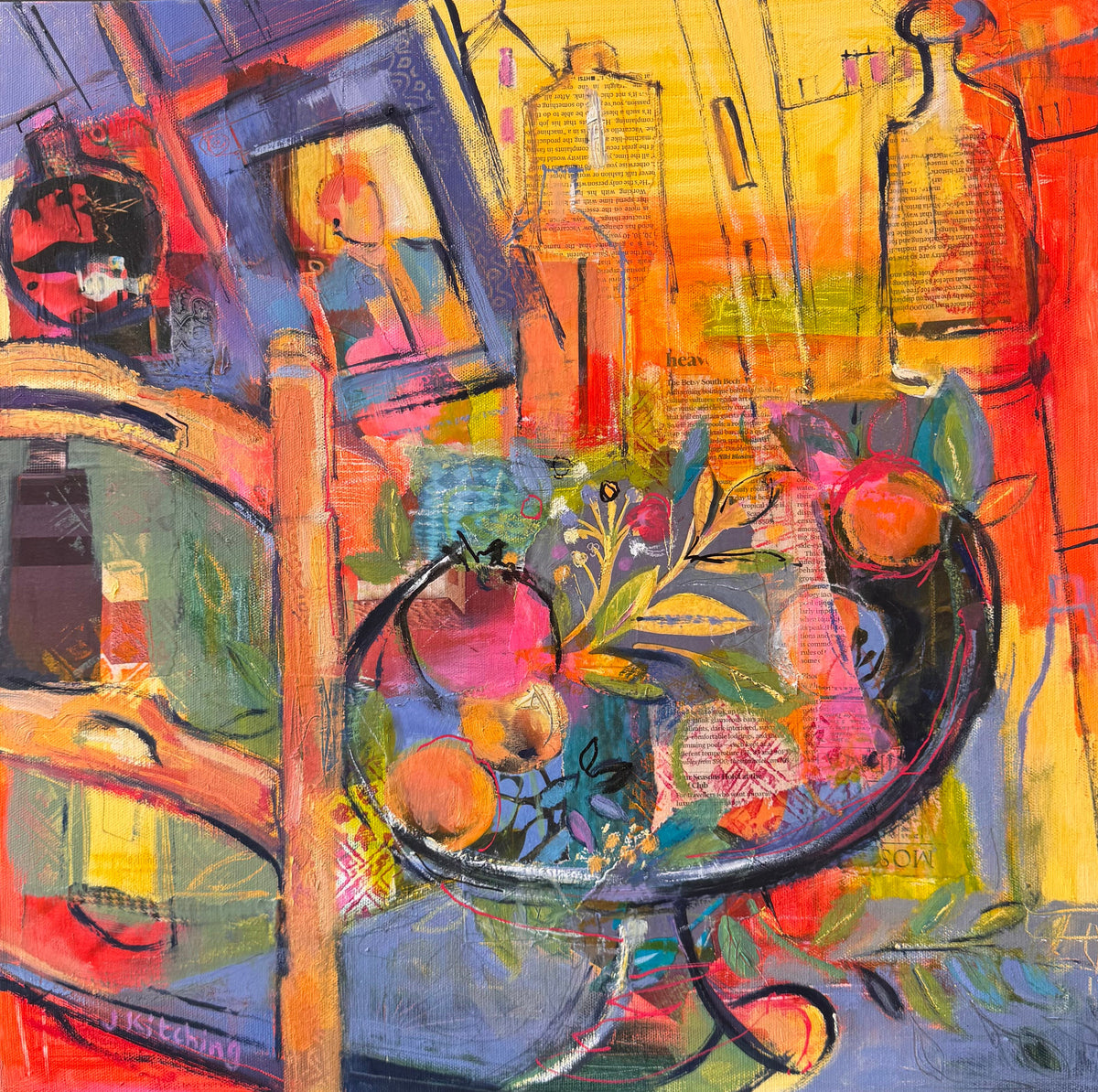 A framed abstract still life painting featuring a bowl of fruit, bottles, and painterly figures, rendered in vivid reds, yellows, blues, greens, and oranges, shown in a black frame on a wooden surface.