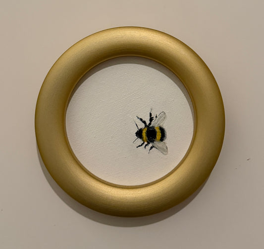 Small painting of a bee inside a gold circular frame on a beige background