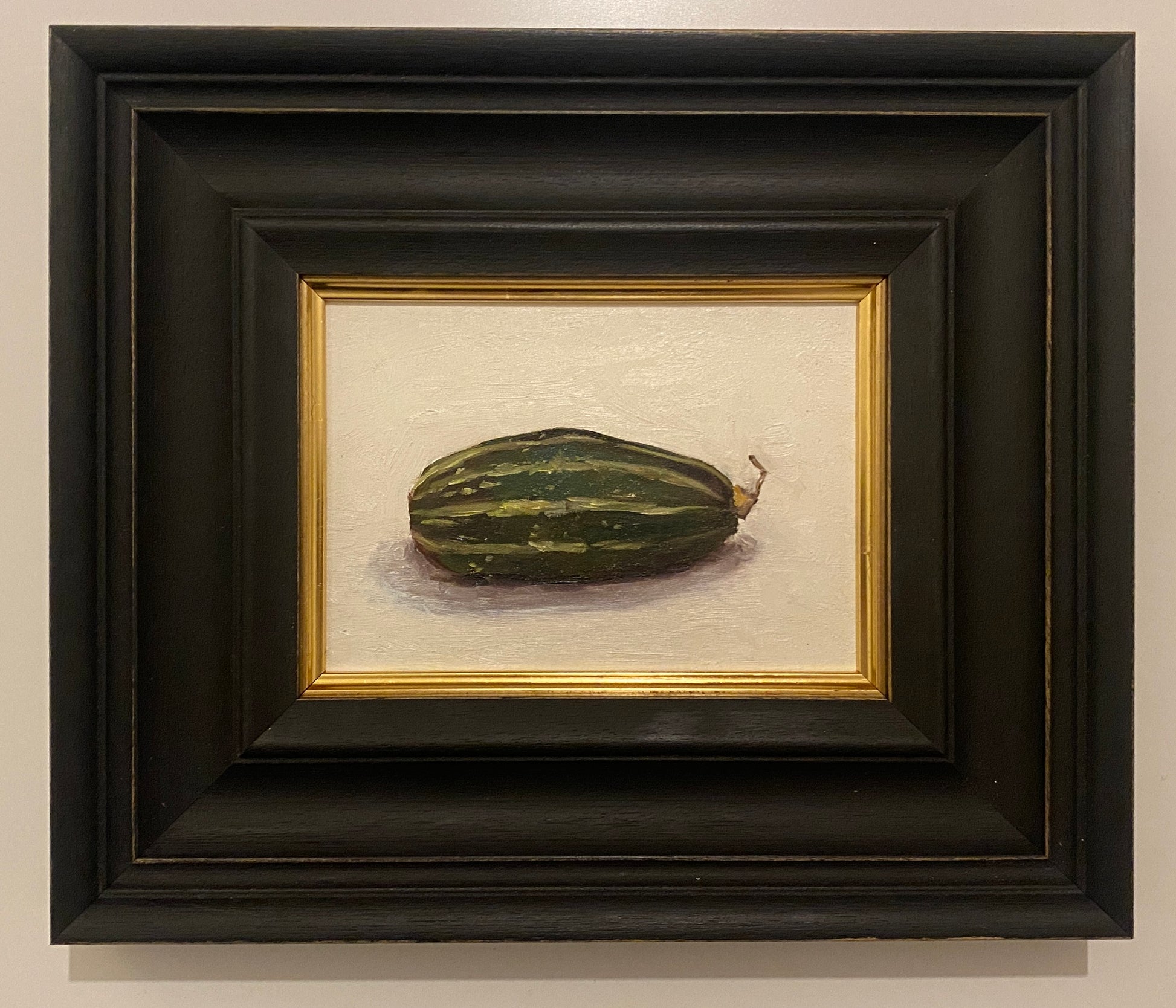 Framed still life painting of a zucchini or gourd on a beige background