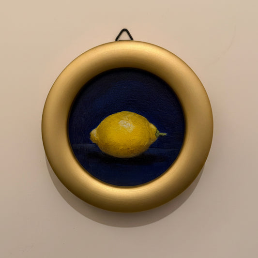 Yellow lemon in a round gold frame on a beige wall