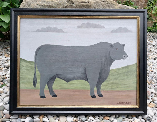 Framed artwork of a bull with a green hill background and blue sk with clouds.