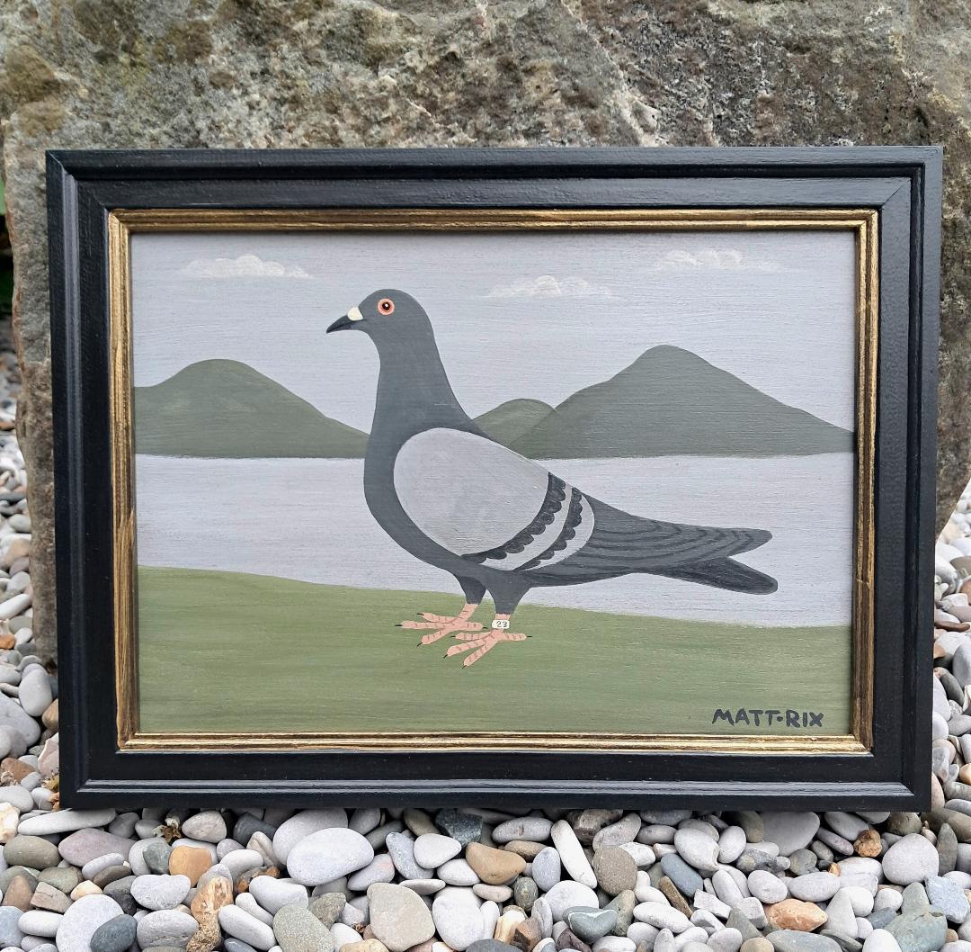 Framed painting of a pigeon with a landscape background, placed on pebbles.