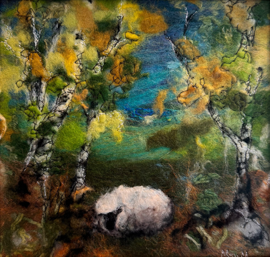 A framed felt painting depicting a white sheep grazing among birch trees with green, yellow, and blue foliage, set in a light wood frame.