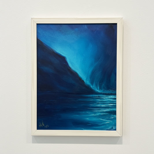 Framed abstract seascape painting with blue and black colors on a white wall.