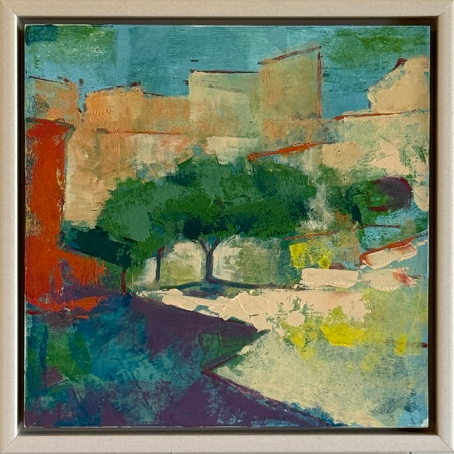 An abstract painting of a Mediterranean-style village scene with stucco buildings, green trees, and a blue sky, housed in a light-colored wooden frame.