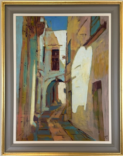 Framed painting of a narrow European alleyway with warm-toned buildings, a blue sky, and a stone path, shown in a gold and gray frame.